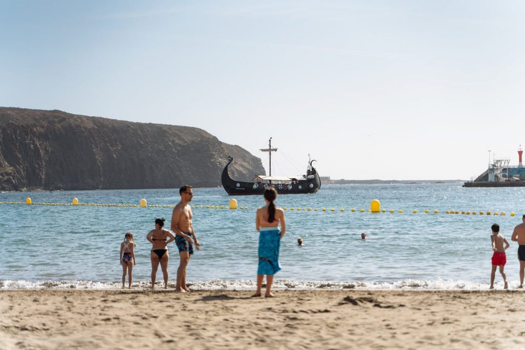 pexels-photo-30327831 A family enjoys a sunny day at a Canary Islands beach with a Viking ship nearby.